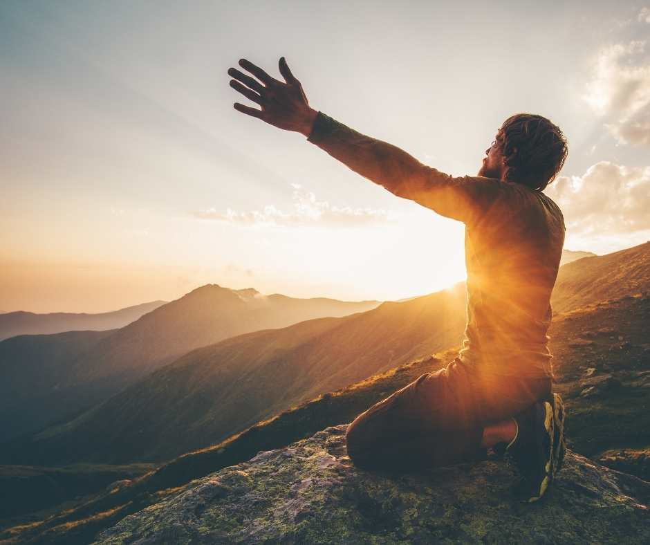 Man with arms outstretched towards setting sun on a mountain ridge.