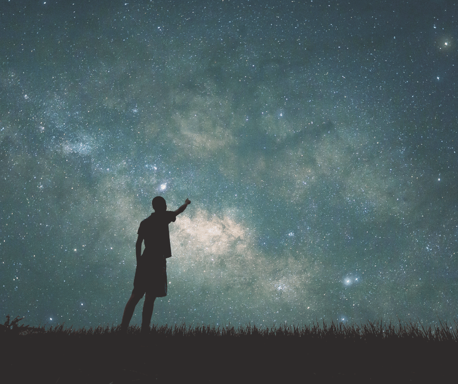 A guy pointing and looking towards the night sky with a blanket of stars!